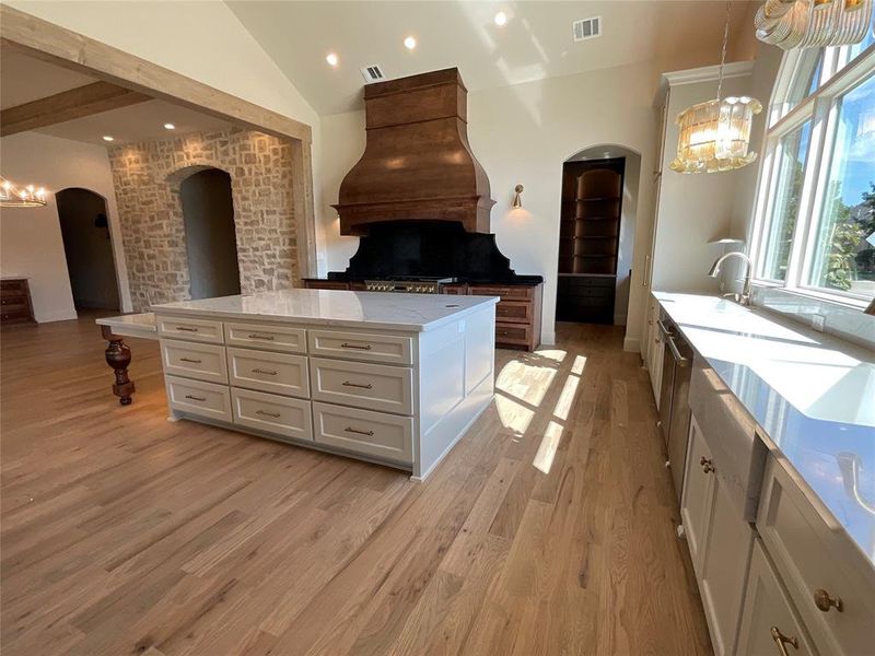 Kitchen featuring white cabinets, pendant lighting, a kitchen island, vaulted ceiling, and light hardwood / wood-style floors