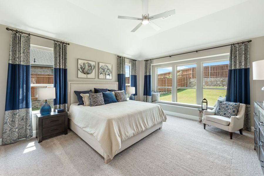 Spacious master bedroom with king bed, ceiling fan, carpet, and large windows with blue curtains