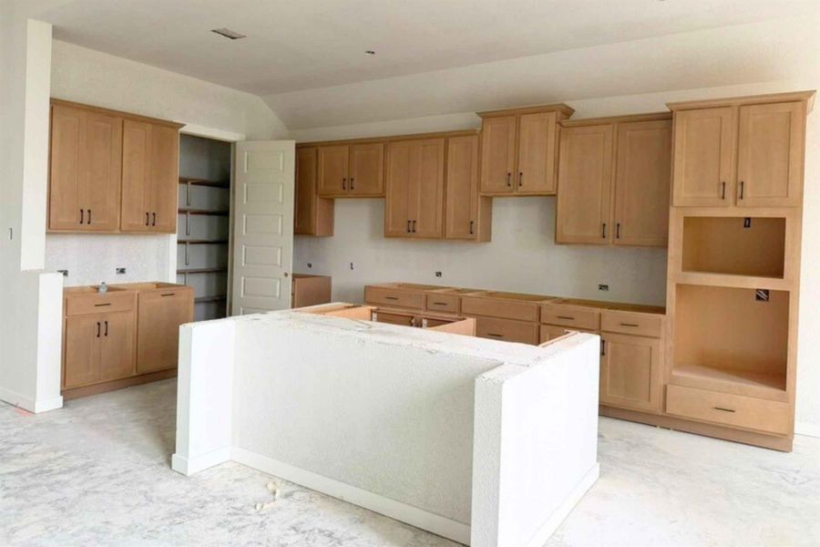 Kitchen with a center island, vaulted ceiling, light wood finish cabinetry, and concrete floors