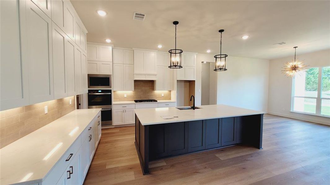 Contemporary kitchen featuring an oversized island with a black base, light countertops, and wood-finish flooring