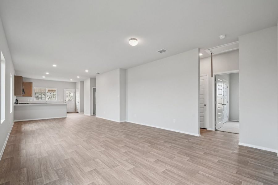 Image of a living room with light grey walls, vinyl flooring and a kitchen in the distance