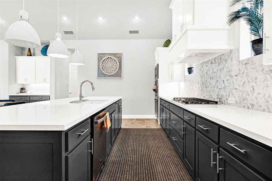 Kitchen featuring tasteful backsplash, dark cabinets, hanging light fixtures, a kitchen island with sink, and white cabinetry Kitchen featuring tasteful backsplash, dark cabinets, hanging light fixtures, a kitchen island with sink, and white cabinetry
