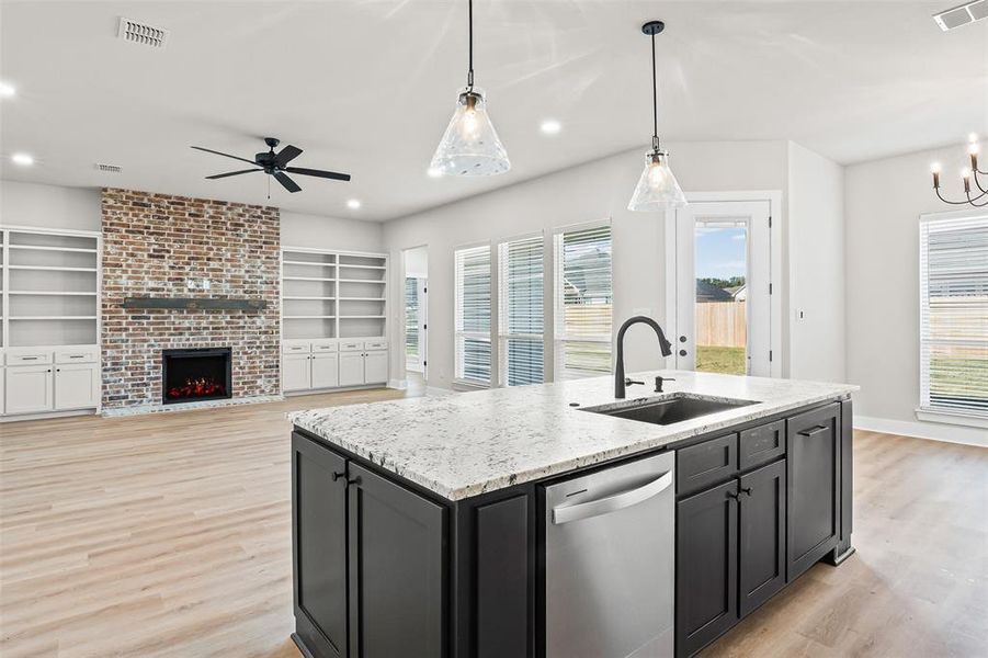 Kitchen featuring dark cabinets, light stone countertops, a center island with sink, dishwasher, and pendant lighting Kitchen featuring dark cabinets, light stone countertops, a center island with sink, dishwasher, and pendant lighting