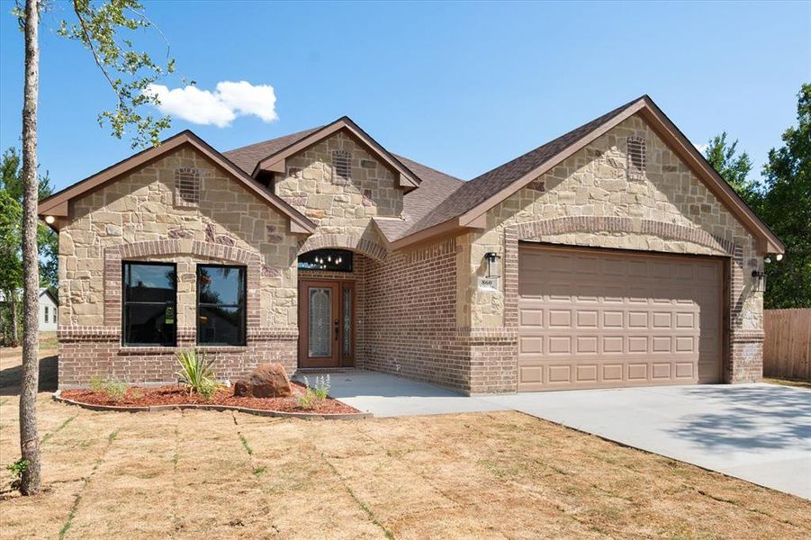 Stone and brick facade featuring an arched entry, decorative front door, and a two-car garage