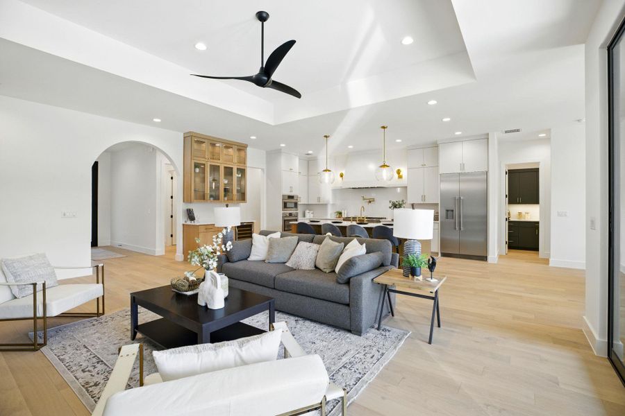 Living area with arched walkways, a ceiling fan, a raised ceiling, light wood-style flooring, and recessed lighting