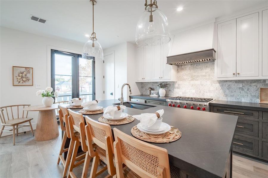 Kitchen with light wood-type flooring, white cabinetry, hanging light fixtures, and sink