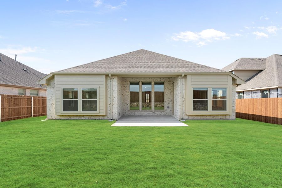 Rear exterior of single-story home with brick and siding, covered patio, and fenced backyard with green lawn Rear exterior of single-story home with brick and siding, covered patio, and fenced backyard with green lawn