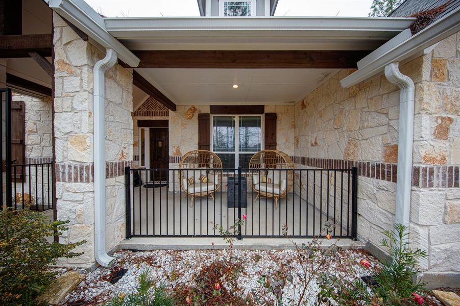 Charming stone patio with cozy seating, enclosed by a decorative metal railing. Ideal for relaxing outdoors, it features rustic stone walls and a covered ceiling for added comfort.