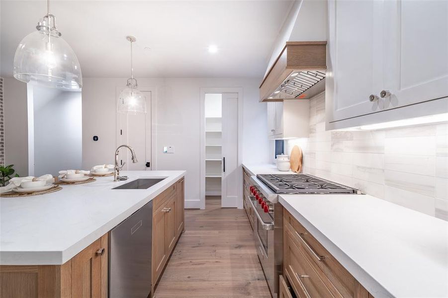 Kitchen with decorative light fixtures, sink, decorative backsplash, stainless steel appliances, and a center island with sink