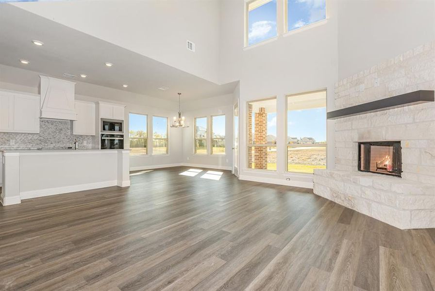 Unfurnished living room with a fireplace, healthy amount of natural light, a chandelier, a towering ceiling, and dark wood-style flooring