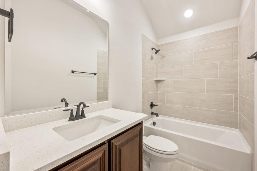 Bathroom with dark wood vanity, quartz countertop, and tiled tub-shower combo with dark metal fixtures