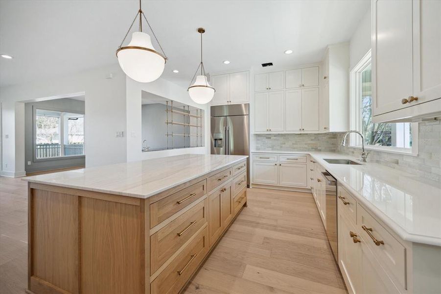 An alternate view of the kitchen highlights its meticulous design and functionality. The oversized island stands out with warm wood tones, topped with a sleek quartz surface, offering ample storage and workspace. Soft-close drawers with brass hardware enhance both style and practicality.