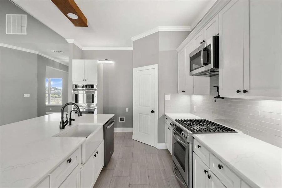 Kitchen with white cabinets, stainless steel appliances, light stone countertops, crown molding, and tasteful backsplash