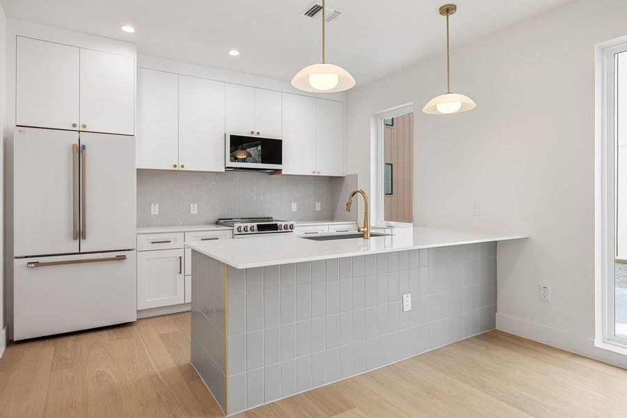 Kitchen with white appliances, light wood-style floors, white cabinetry, and a peninsula