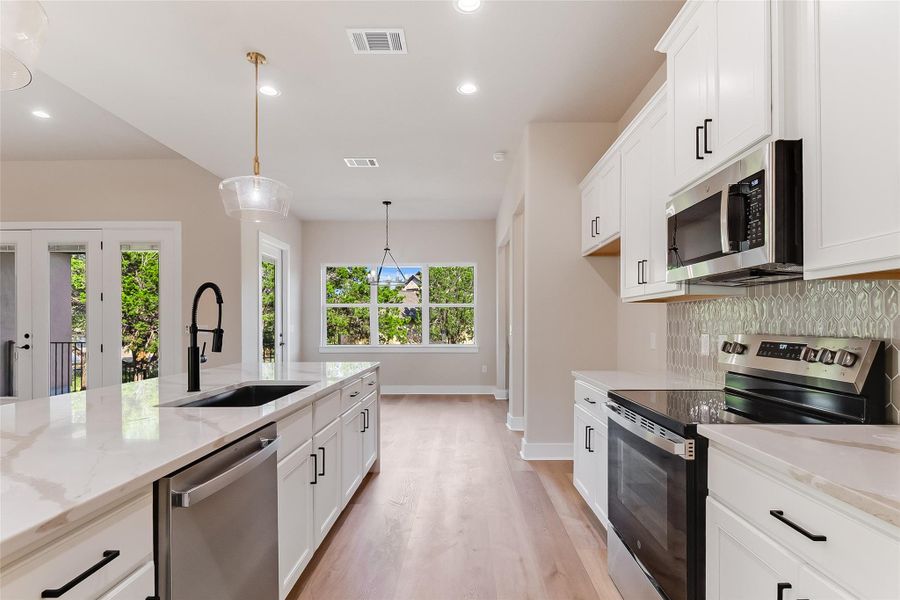 Kitchen featuring stainless steel appliances, white cabinetry, light wood finished floors, light stone counters, and recessed lighting Kitchen featuring stainless steel appliances, white cabinetry, light wood finished floors, light stone counters, and recessed lighting