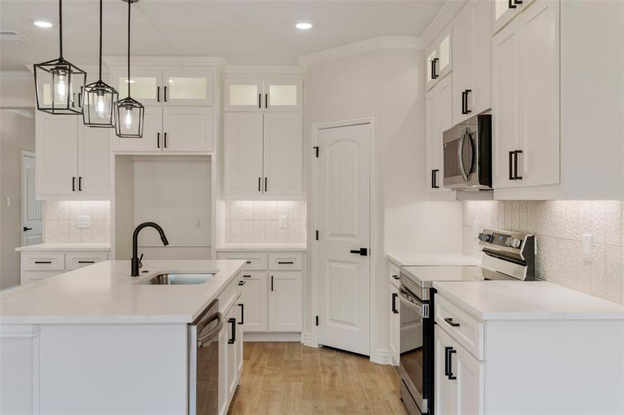 Kitchen with white cabinetry, stainless steel appliances, sink, and a center island with sink