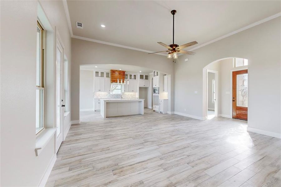 Unfurnished living room with light hardwood / wood-style flooring, ceiling fan, and crown molding