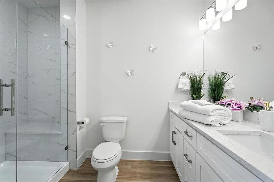 Bathroom featuring a marble finish shower, light wood-style floors, and double vanity