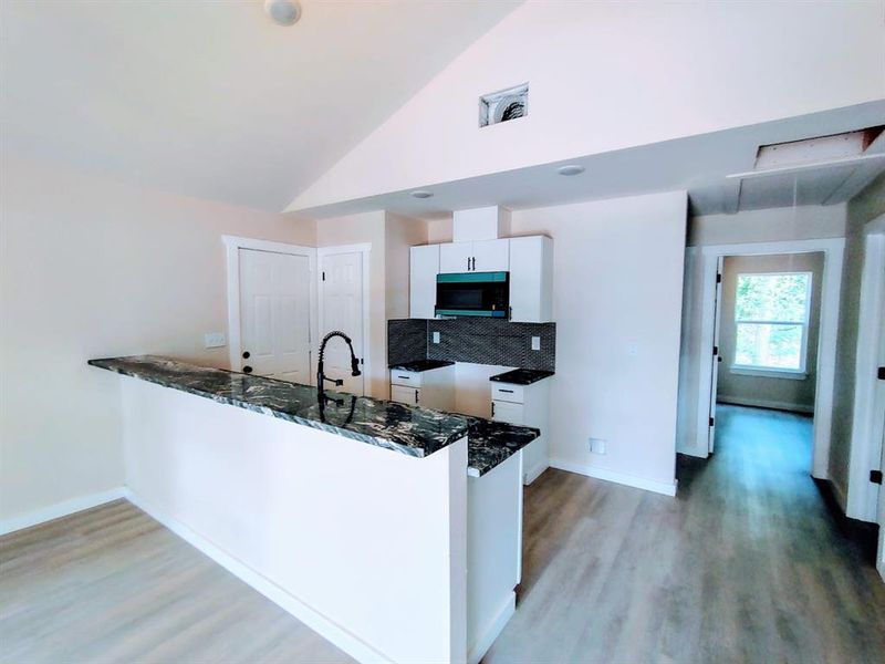 Kitchen featuring black microwave, dark stone counters, a peninsula, white cabinetry, and light wood-style floors
