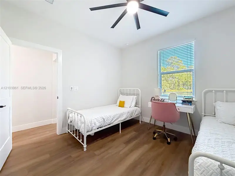 Room featuring wood-finish flooring, a matte black multi-blade ceiling fan, and a single-hung window with integrated horizontal blinds
