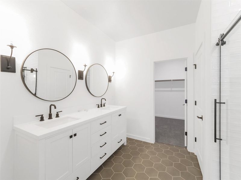 Modern primary bathroom with dual sinks, round mirrors, and sleek fixtures. Features hexagonal floor tiles and a spacious walk-in closet. Bright and minimalist design.