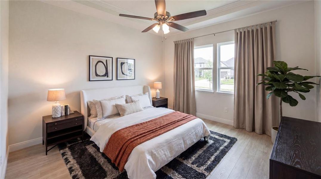 Spacious bedroom featuring wood-finish flooring, a tray ceiling, and a ceiling fan with integrated lighting