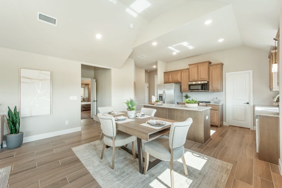 Open dining area with wood table and four chairs, adjacent to kitchen with wood cabinets and stainless appliances