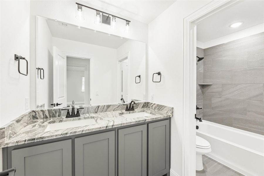 Bathroom with double vanity, gray cabinets, marble countertop, and tiled shower-tub combo Bathroom with double vanity, gray cabinets, marble countertop, and tiled shower-tub combo