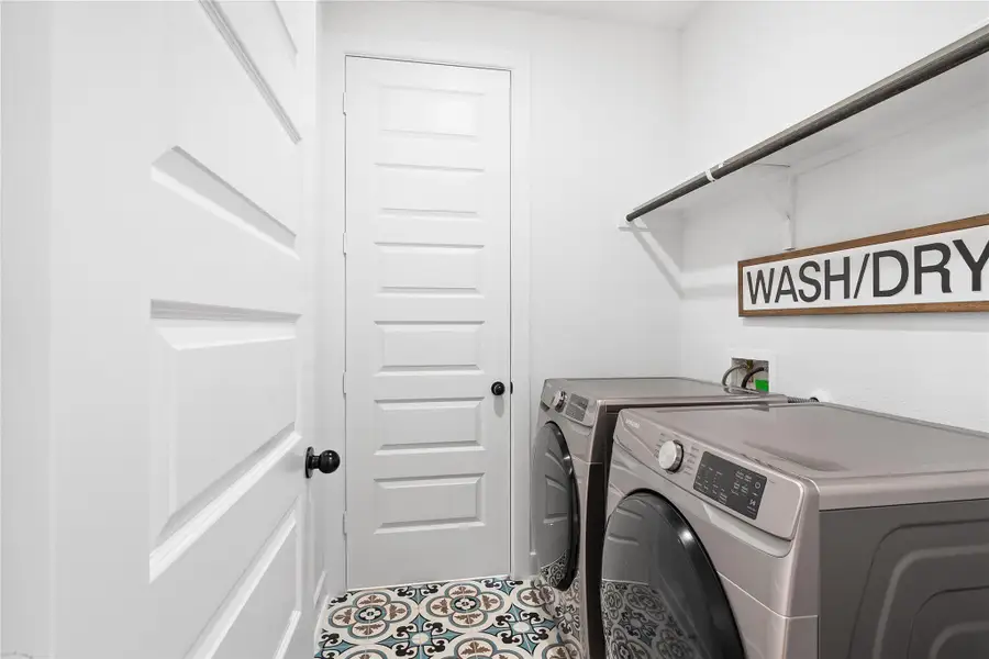 Utility room featuring decorative floor tiling, a white wall shelf, and a hanging rod Utility room featuring decorative floor tiling, a white wall shelf, and a hanging rod