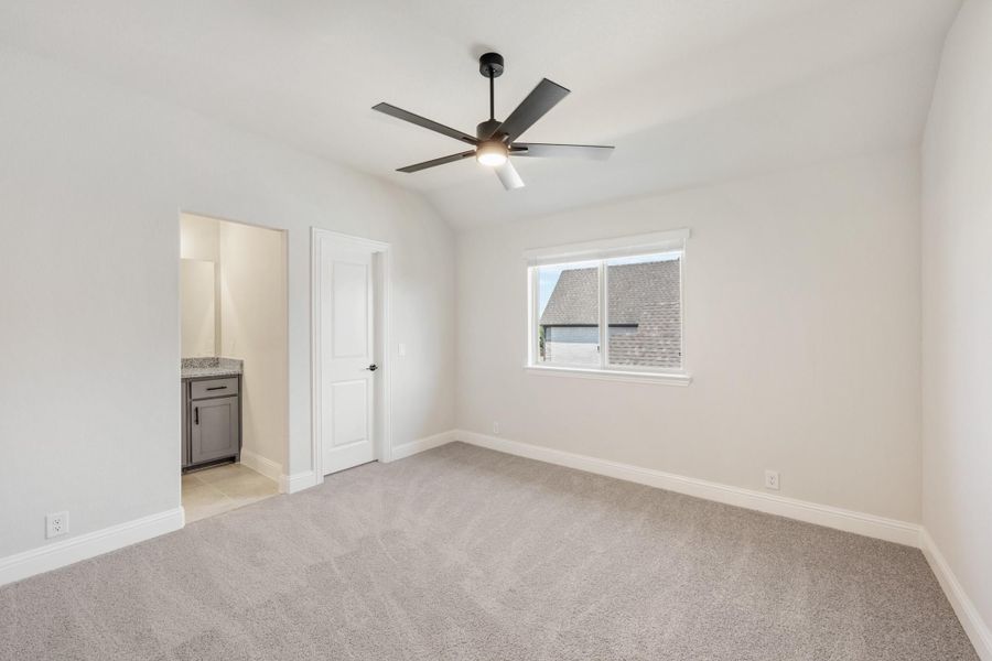 Bedroom with vaulted ceiling, ceiling fan, carpet flooring, and ensuite bathroom entrance
