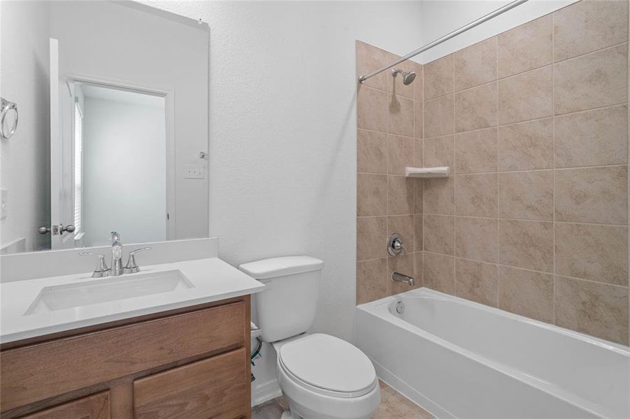 Secondary bath features tile flooring, bath/shower combo with tile surround, stained wood cabinets, beautiful light countertops, mirror, sleek fixtures and modern finishes.