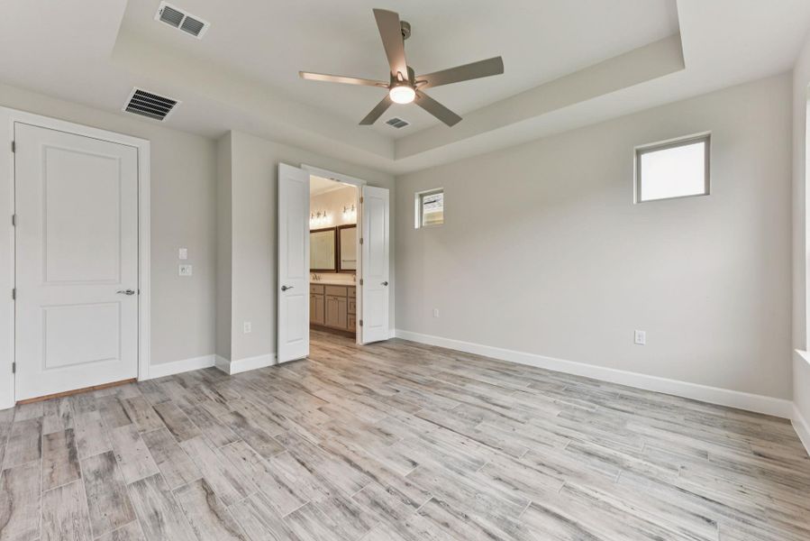 Unfurnished bedroom featuring a raised ceiling, ceiling fan, connected bathroom, and light wood-type flooring
