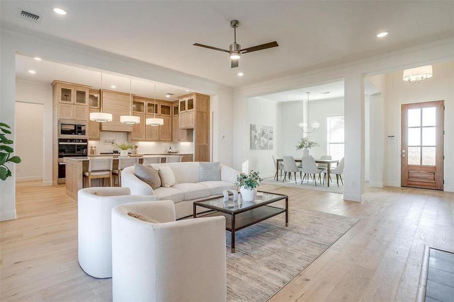 Living room with ceiling fan with notable chandelier, light hardwood / wood-style flooring, and crown molding