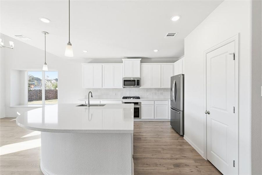 Kitchen featuring white cabinetry, tasteful backsplash, pendant lighting, a center island with sink, and stainless steel appliances