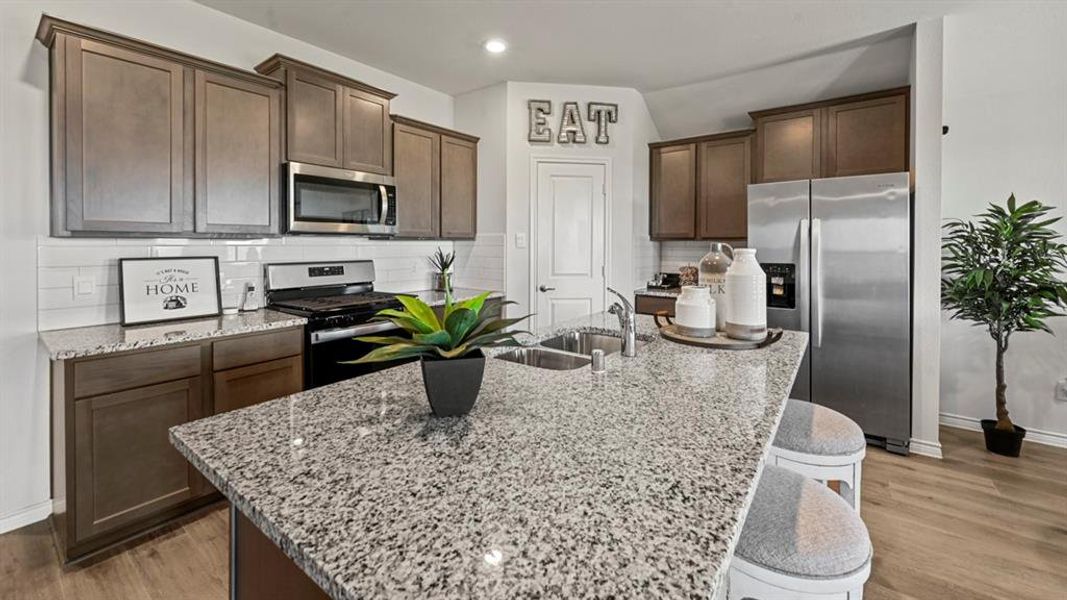 Kitchen featuring dark brown cabinetry, appliances with stainless steel finishes, light stone countertops, a breakfast bar, and light wood-style floors