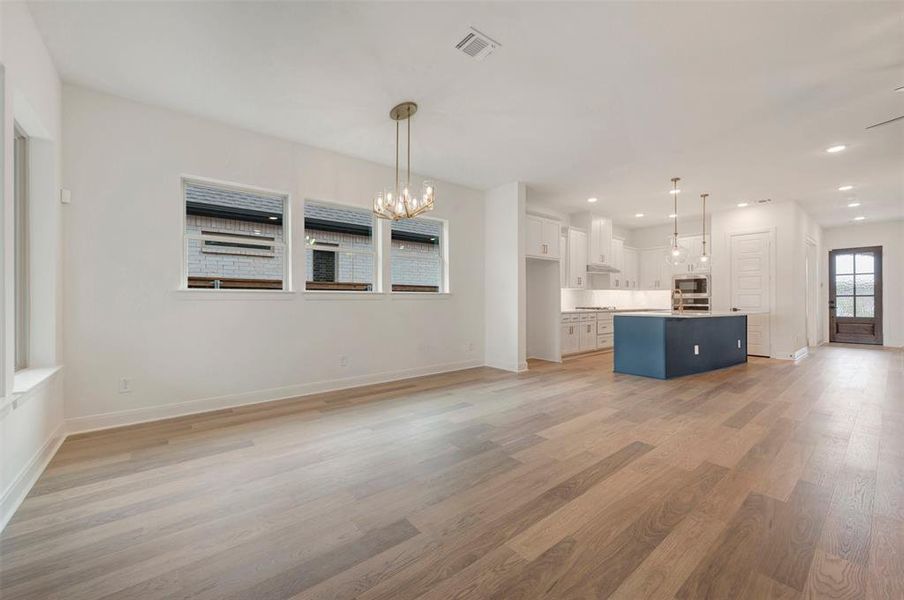 Open concept living space featuring light wood-style flooring, a modern chandelier, and a bright white kitchen with a blue island