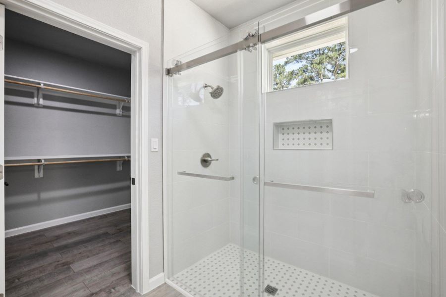 Full bathroom with a shower stall, light wood-type laminate flooring, and a walk in closet