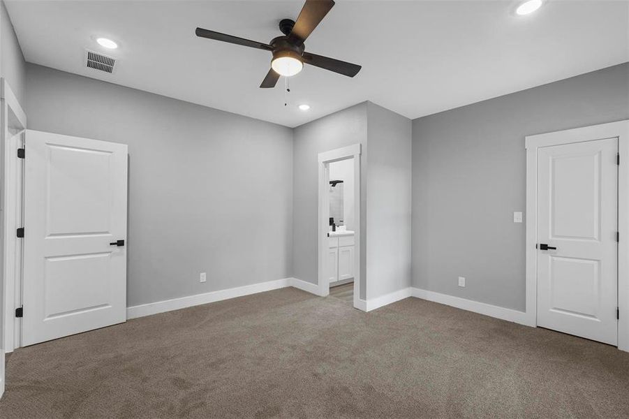 Unfurnished bedroom featuring ceiling fan, ensuite bath, and light carpet