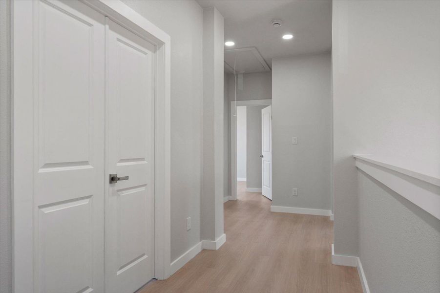 A naturally illuminated hallway with recessed lighting and light hardwood flooring creates a welcoming flow.