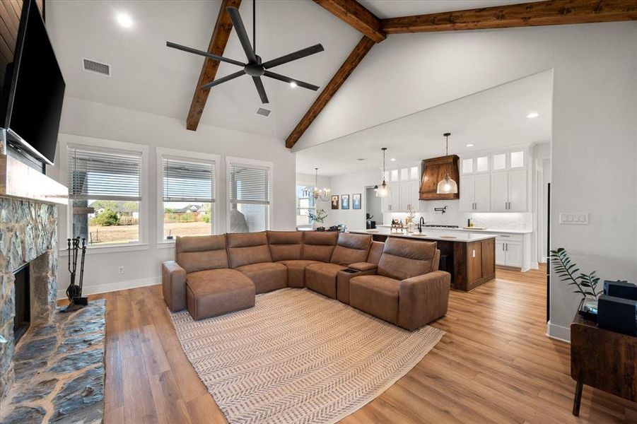 Living area featuring light wood finished floors, high vaulted ceiling, a fireplace, beamed ceiling, and recessed lighting