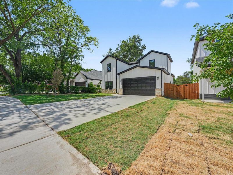 Modern farmhouse exterior featuring black trim accents, a two-car garage with a dark panel door, board and batten siding, and stone detailing Modern farmhouse exterior featuring black trim accents, a two-car garage with a dark panel door, board and batten siding, and stone detailing