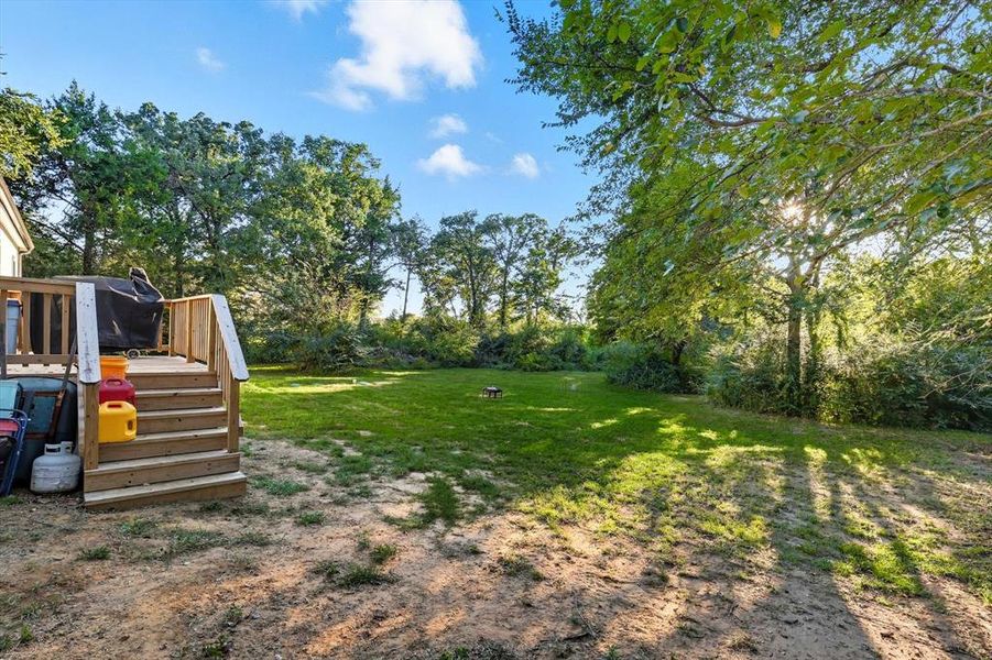 View of grassy yard featuring a deck, a playground, and view of scattered trees View of grassy yard featuring a deck, a playground, and view of scattered trees