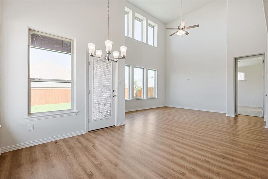 Unfurnished dining area with ceiling fan with notable chandelier, light hardwood / wood-style flooring, and high vaulted ceiling