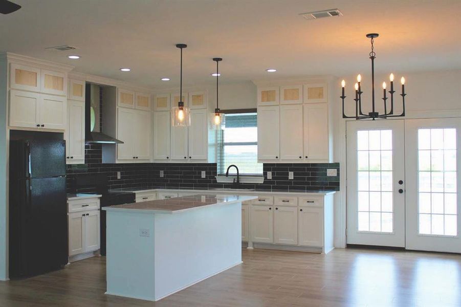 Kitchen with french doors, freestanding refrigerator, tasteful backsplash, wall chimney range hood, and a kitchen island Kitchen with french doors, freestanding refrigerator, tasteful backsplash, wall chimney range hood, and a kitchen island