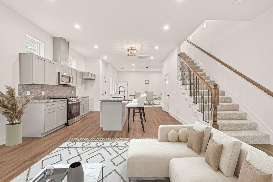 This modern open-plan living space features a sleek kitchen with gray cabinets and stainless steel appliances, an island with bar seating, and a cozy lounge area. The engineer wood floors and neutral tones create a warm ambiance, complemented by a stylish staircase leading to the upper level.- Virtual Staging This modern open-plan living space features a sleek kitchen with gray cabinets and stainless steel appliances, an island with bar seating, and a cozy lounge area. The engineer wood floors and neutral tones create a warm ambiance, complemented by a stylish staircase leading to the upper level.- Virtual Staging