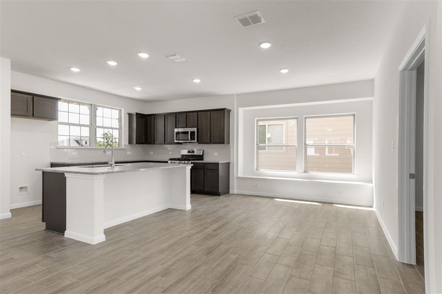 Kitchen with decorative backsplash, a center island with sink, light wood-style floors, visible vents, and appliances with stainless steel finishes
