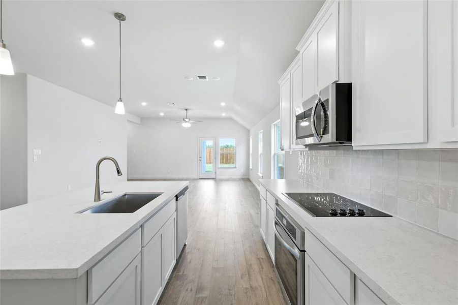 Kitchen featuring a center island with sink, lofted ceiling, white cabinets, recessed lighting, and light wood finished floors Kitchen featuring a center island with sink, lofted ceiling, white cabinets, recessed lighting, and light wood finished floors