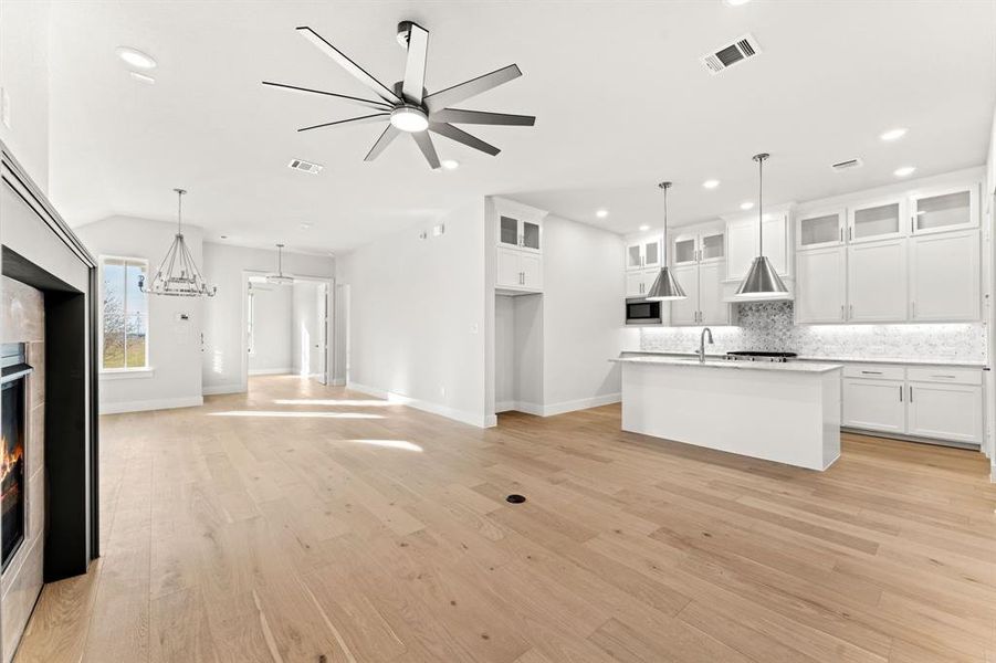 Kitchen with pendant lighting, a center island with sink, white cabinetry, and a fireplace