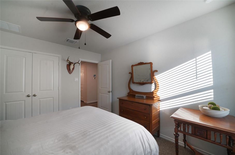 Bedroom with dark colored carpet, ceiling fan, and a closet