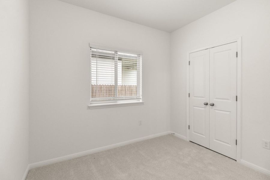 This room offers light-colored carpet, a window with horizontal blinds, and a white bi-fold door